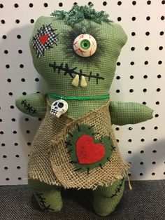 a green stuffed animal with a red heart on it's chest and two eyes