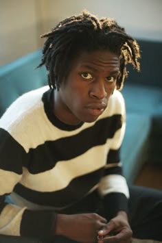 a young man with dreadlocks sitting on a couch looking at his cell phone