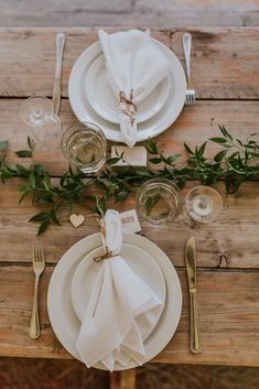 the place setting is set with white plates and napkins, silverware, and greenery