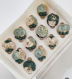 twelve cupcakes with frosting and decorations in a white box on a table