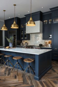 a large kitchen with blue cabinets and gold pendant lights hanging from the ceiling, along with two bar stools