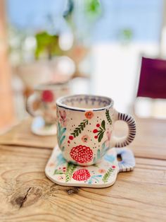 two coffee cups sitting on top of a wooden table next to another cup and saucer