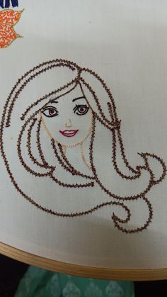 a woman's face is drawn on a white piece of cloth with brown thread