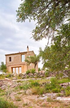 an old stone house in the middle of a field with rocks and trees around it