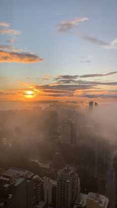 the sun is setting over a city with tall buildings and skyscrapers in the fog