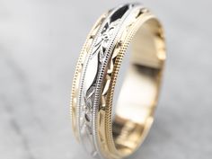 two tone gold and silver wedding band with intricate engraving on the sides, set against a marble background