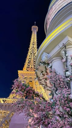 the eiffel tower lit up at night with pink flowers in front of it