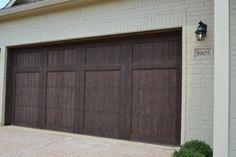 a brown garage door in front of a white brick building with an address sign on it