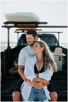 a man and woman sitting on the back of a truck with their arms around each other