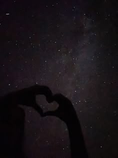 the silhouette of a person making a heart shape with their hands under the stars in the night sky