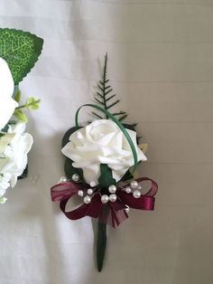 a boutonniere with white flowers and green leaves on the wall next to another bouquet