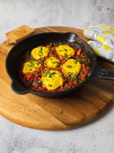 an iron skillet filled with eggs on top of a wooden cutting board next to bread