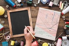 a person is drawing on a blackboard surrounded by sewing supplies