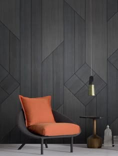 an orange chair sits in front of a black wall with geometric designs on it and a small table next to it