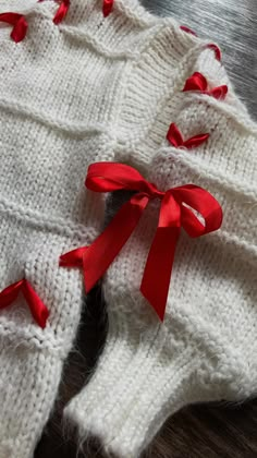 two white knitted sweaters with red bows on the top and bottom, sitting on a table