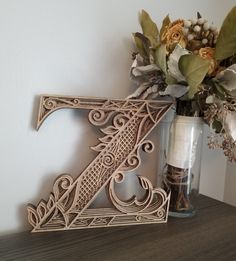 a decorative wooden letter sitting next to a vase with flowers