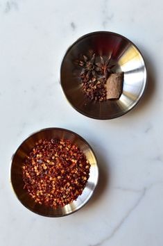 two metal bowls filled with spices on top of a white counter