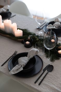 the table is set with black plates and silverware, candles, and greenery