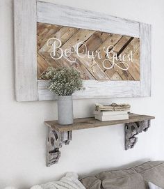 a wooden sign that says be our guest above a shelf with books and flowers on it