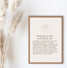 a framed poster with the words welcome to this world little one on it next to some dry grass