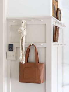 a brown bag hanging on the wall next to a white book shelf with a clock