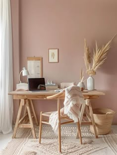 a desk with a laptop on top of it in front of a pink wall and white curtains