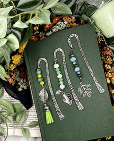 an open book sitting on top of a table next to some green leaves and beads