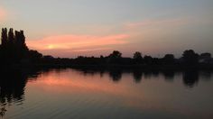 the sun is setting over water with trees in the background