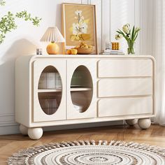 a white cabinet sitting on top of a hard wood floor next to a lamp and potted plant