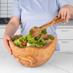 a woman holding a wooden bowl filled with lettuce and tomatoes, as she stirs the salad