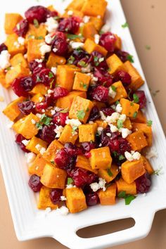 a white platter filled with sweet potatoes and cranberry salad on top of a table