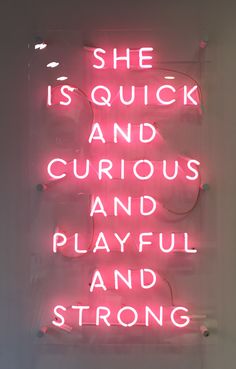 a pink neon sign that says she is quick and curious and playful and strong,