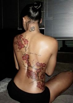 a woman is sitting on the floor with her back turned to the camera and tattoos on her body