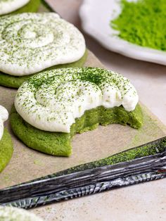 green cookies with white frosting and sprinkles are on a cutting board