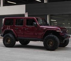 a red jeep is parked in front of a building with two large tires on it