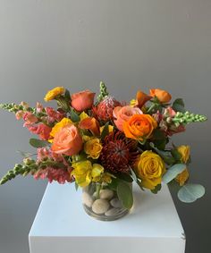 a vase filled with flowers and rocks on top of a white cubed table next to a gray wall