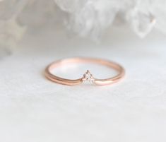 a rose gold ring with a single diamond in the center on a white surface next to some flowers