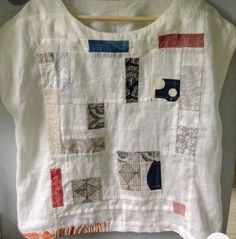 a white shirt with patchwork on it hanging from a clothes hanger in front of a door