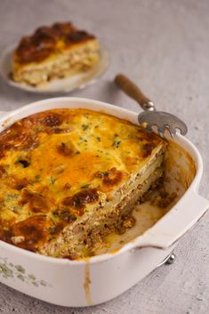 a casserole dish with meat and cheese in it next to a serving utensil