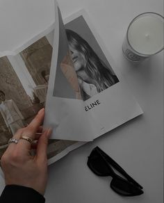 a person holding an open photo book next to a candle and some glasses on a table