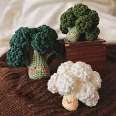 two crocheted broccoli heads sitting next to each other on a bed