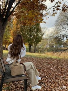 a woman is sitting on a bench in the leaves