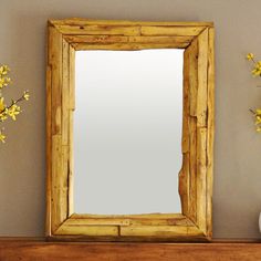 a mirror sitting on top of a wooden shelf next to a vase with yellow flowers