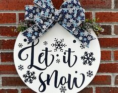 a sign that says let it snow hanging on the side of a brick wall with blue and white bows