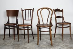 three wooden chairs sitting next to each other in front of a white wall and cement floor