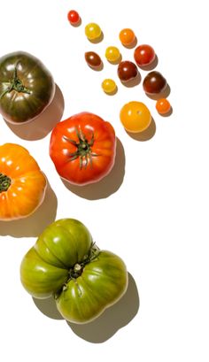 four different types of tomatoes on a white surface with one orange, one green and one red