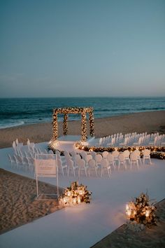 an outdoor ceremony set up on the beach with candles and flowers in front of it