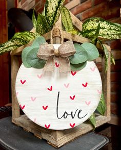 a wooden sign that says love with hearts on it and a bow hanging from the front