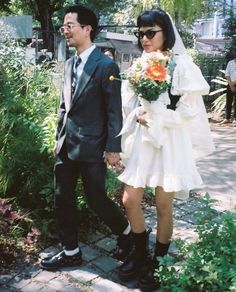 a man and woman dressed up in wedding attire walking down a path with flowers on their bouquets