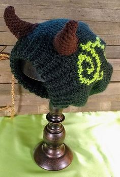 a crocheted hat with horns on top of a metal stand next to a wooden wall